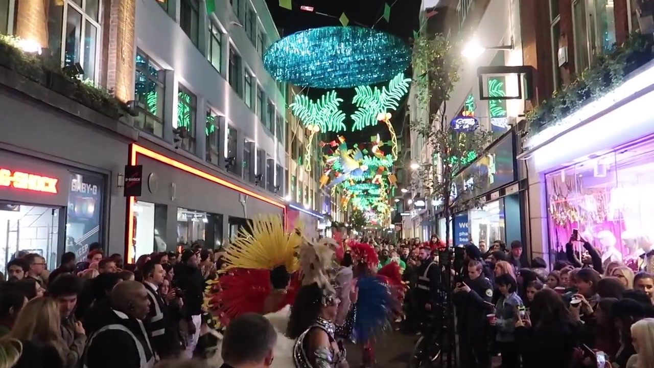 Costumed carnival dancers surrounded by spectators on Carnaby Street.
