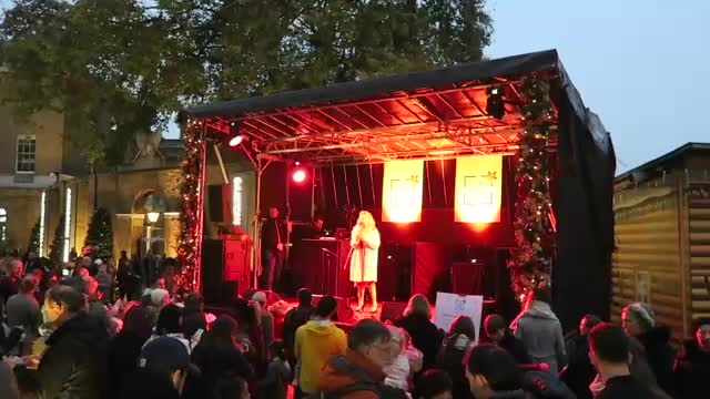 Singer on the red-lit Duke of York Square stage with a crowd in front