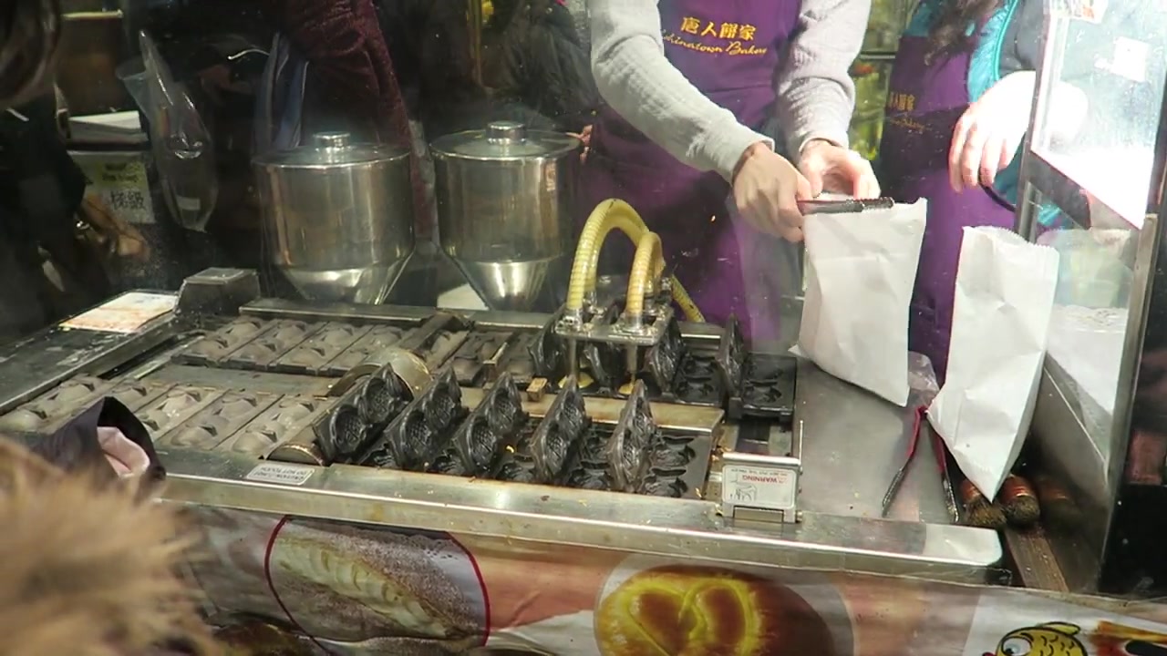 A worker beside the taiyaki machine and paper bags at Chinatown Bakery