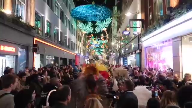 Crowds and a feathered performer beneath colourful Carnaby Street decorations