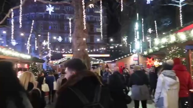 Visitors between wooden Christmas stalls beneath lights in Leicester Square