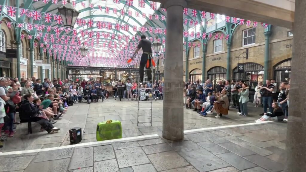 Covent Garden street performer and audience beneath summer decorations in 2022
