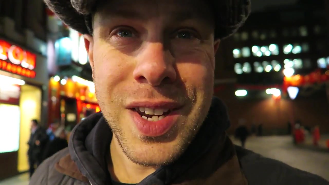 Barry smiling in a flat cap beneath Chinatown lanterns at night