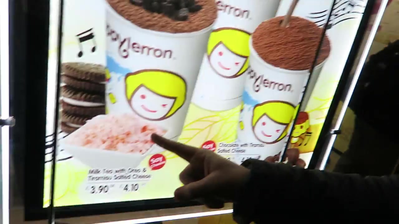 A hand pointing at Happy Lemon milk tea and Oreo drink posters