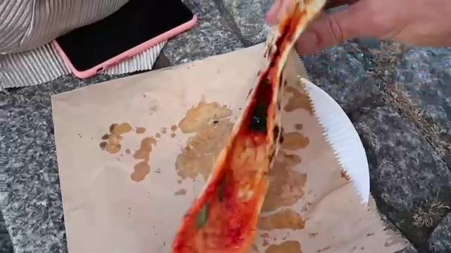 A slice of Homeslice pizza being lifted from its paper plate at Seven Dials