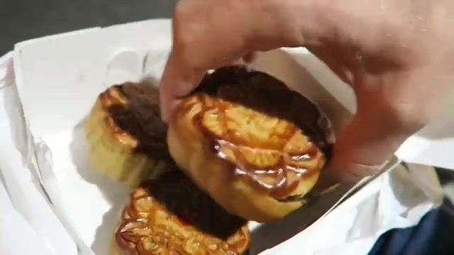 A hand lifting a patterned mooncake from a white bakery box