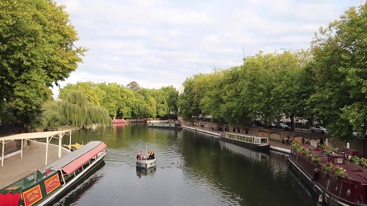 A boat on the water and moored narrowboats viewed from the bridge at Little Venice.