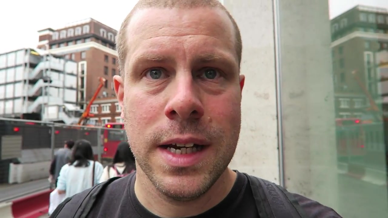Barry talking to the camera while walking past London buses and buildings in 2016