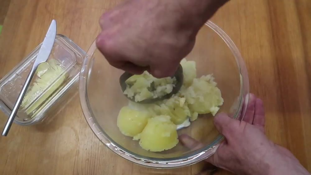 Mashing boiled potatoes with butter in a glass bowl