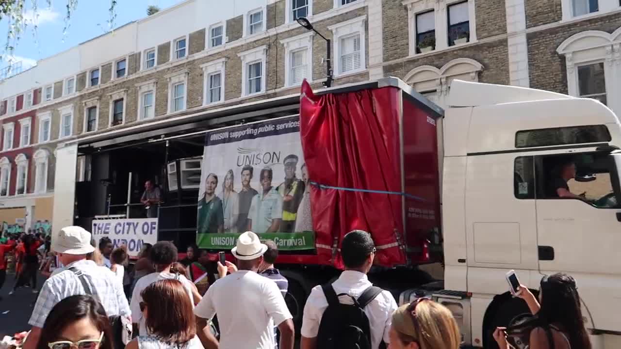 Carnival truck and participants passing spectators beside Notting Hill buildings