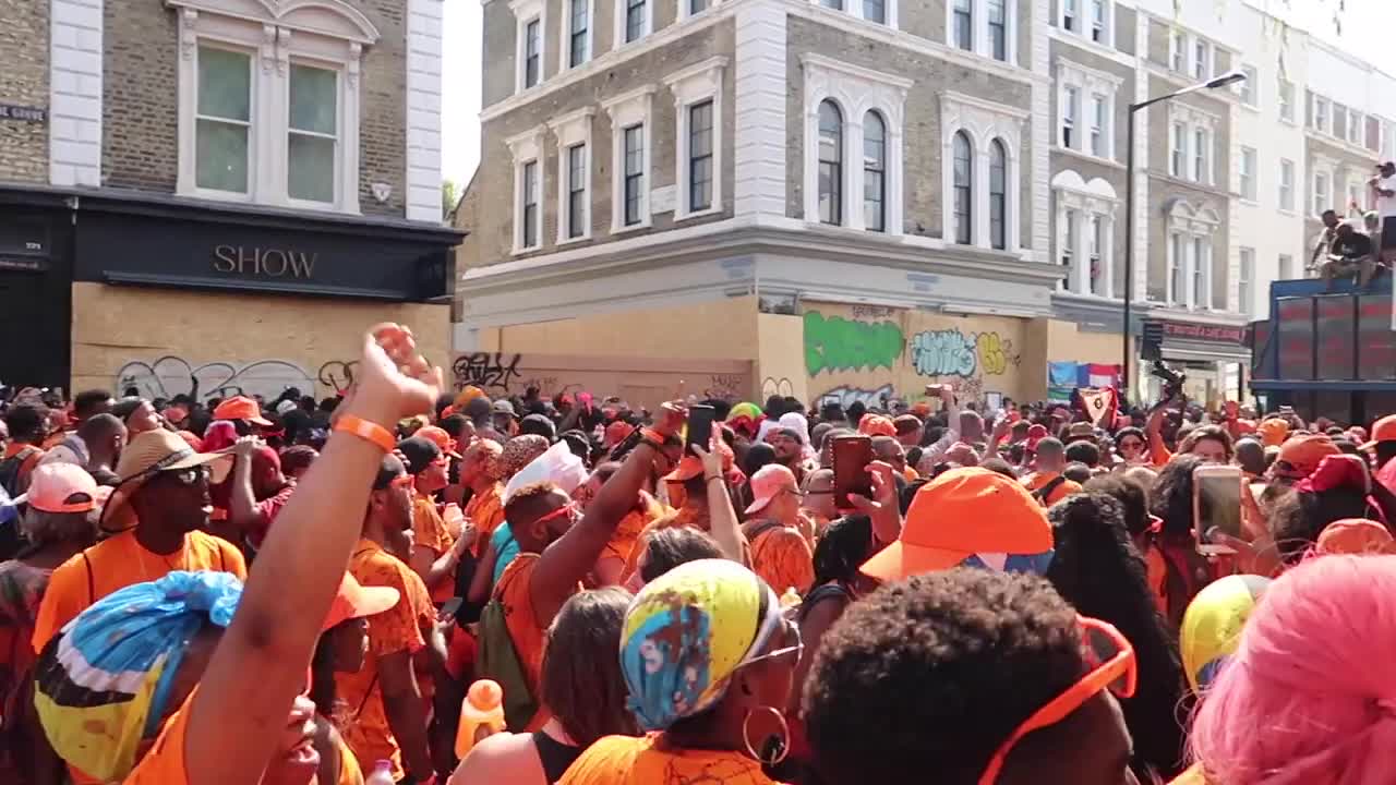 Carnival participants raising their arms and dancing in a crowded Notting Hill street