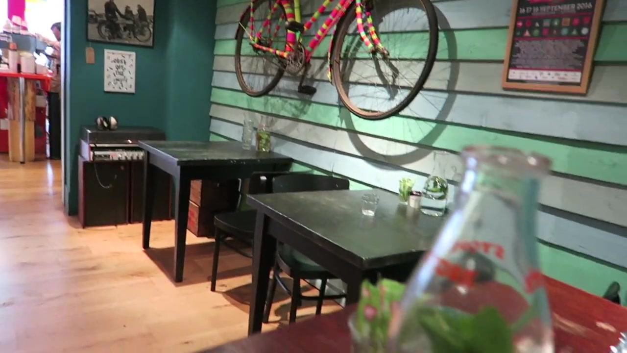 Colourful tables and chairs beneath a bicycle on the wall at Pedlars Notting Hill
