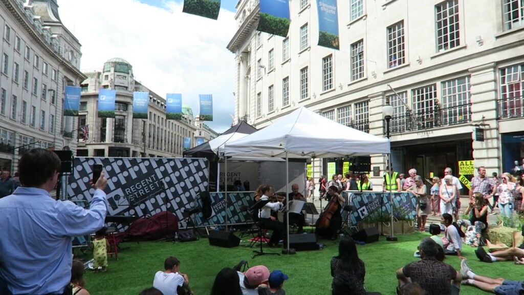 Musicians and spectators beside a bandstand on Regent Street