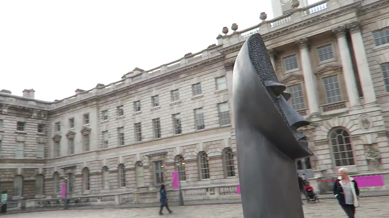 Side view of a tall dark Zak Ové figure against the stone façade of Somerset House