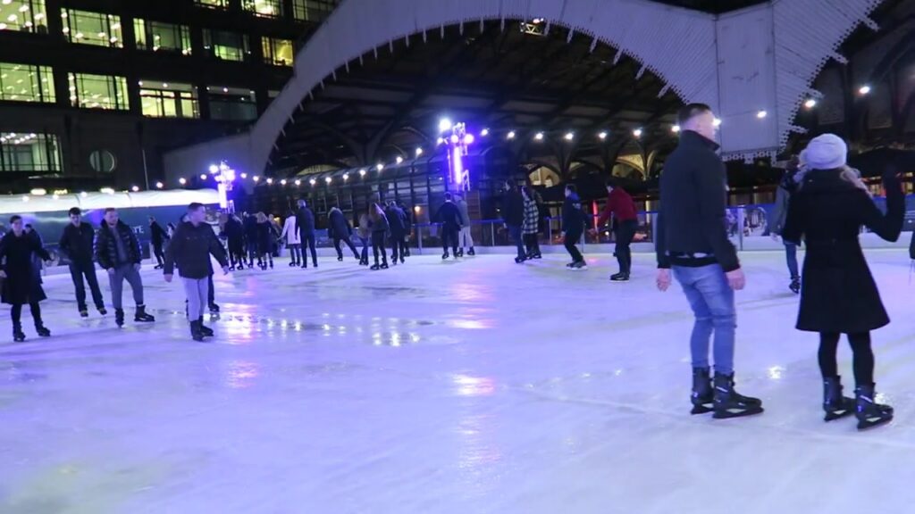 Skaters on the illuminated Broadgate ice rink in Exchange Square at night.