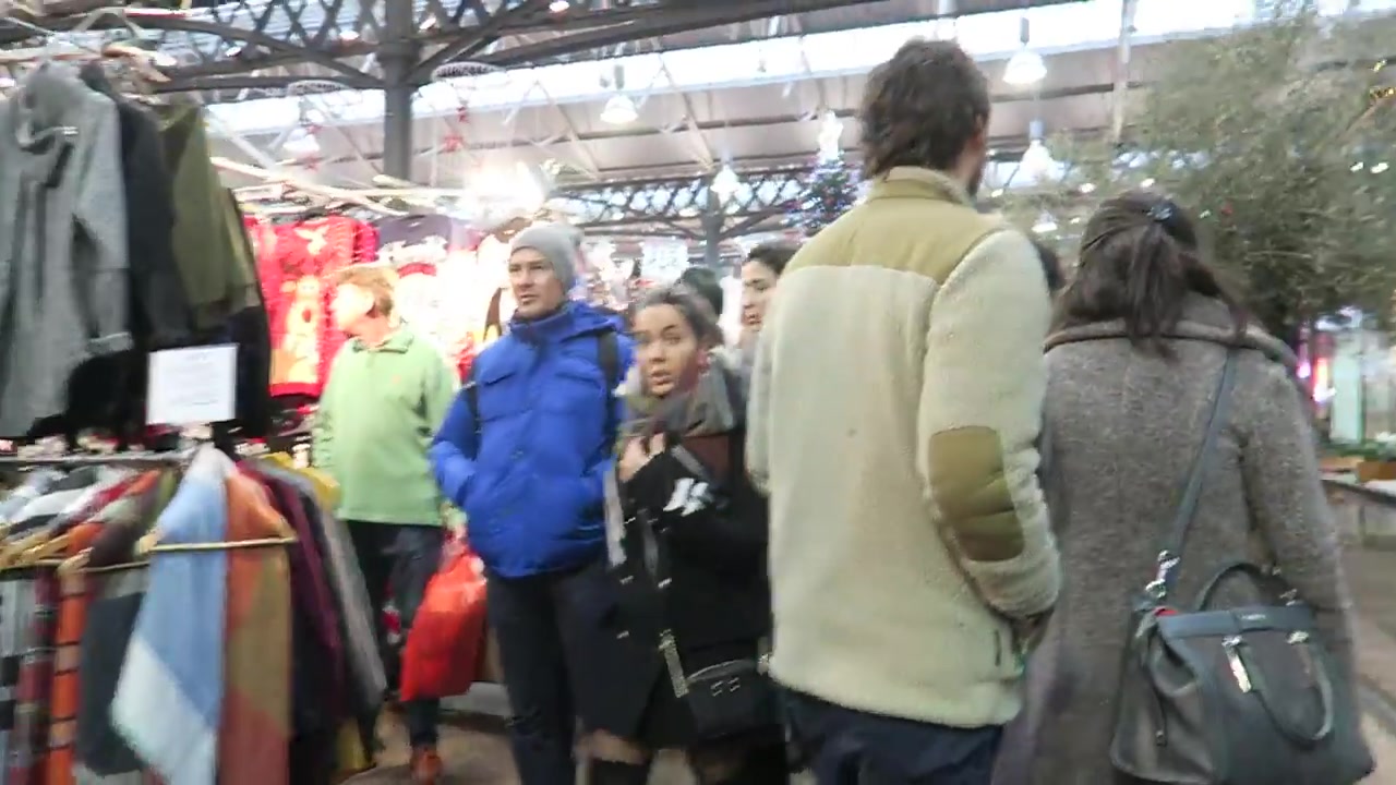 Shoppers browsing clothing stalls inside Old Spitalfields Market.