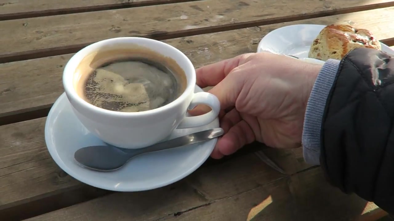 Black coffee and a scone with cream and jam on an outdoor wooden table