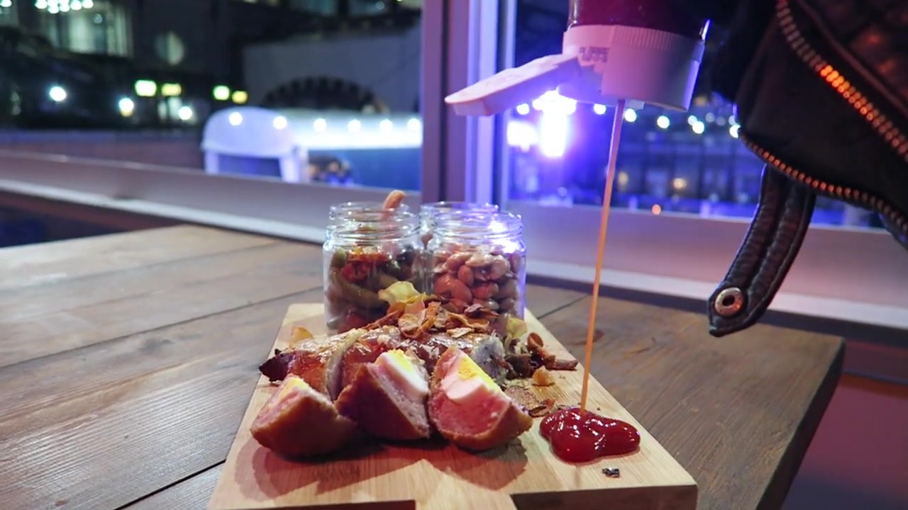 A board of bar snacks and jars of nuts on a wooden table beside the ice rink.