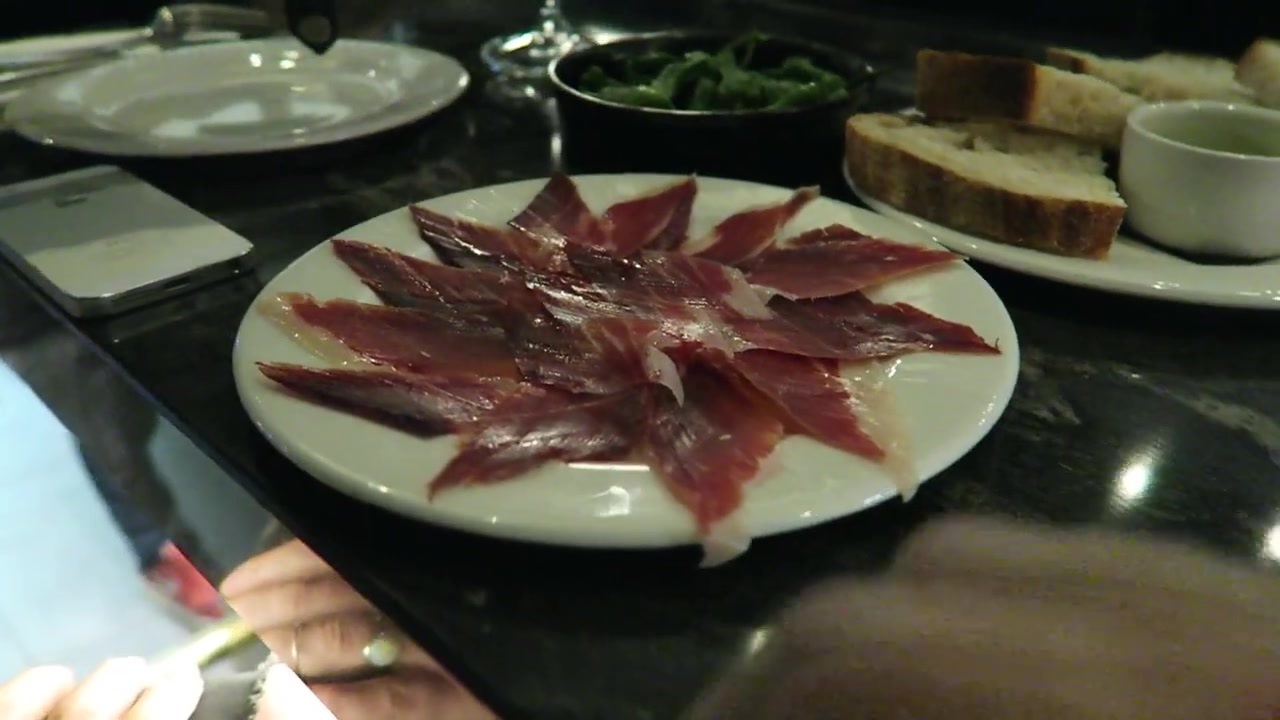 A plate of thinly sliced Ibérico ham with bread and tapas on the table.