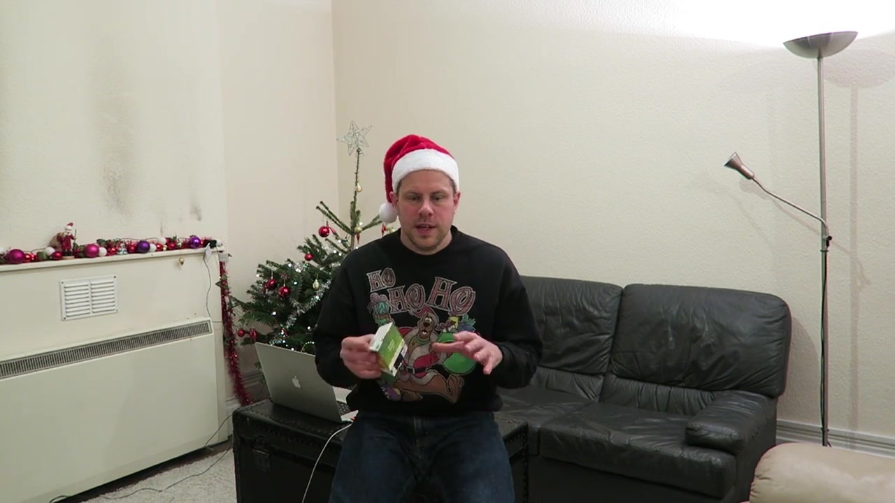 Barry sits beside the Christmas tree holding a packaged Christmas pudding.