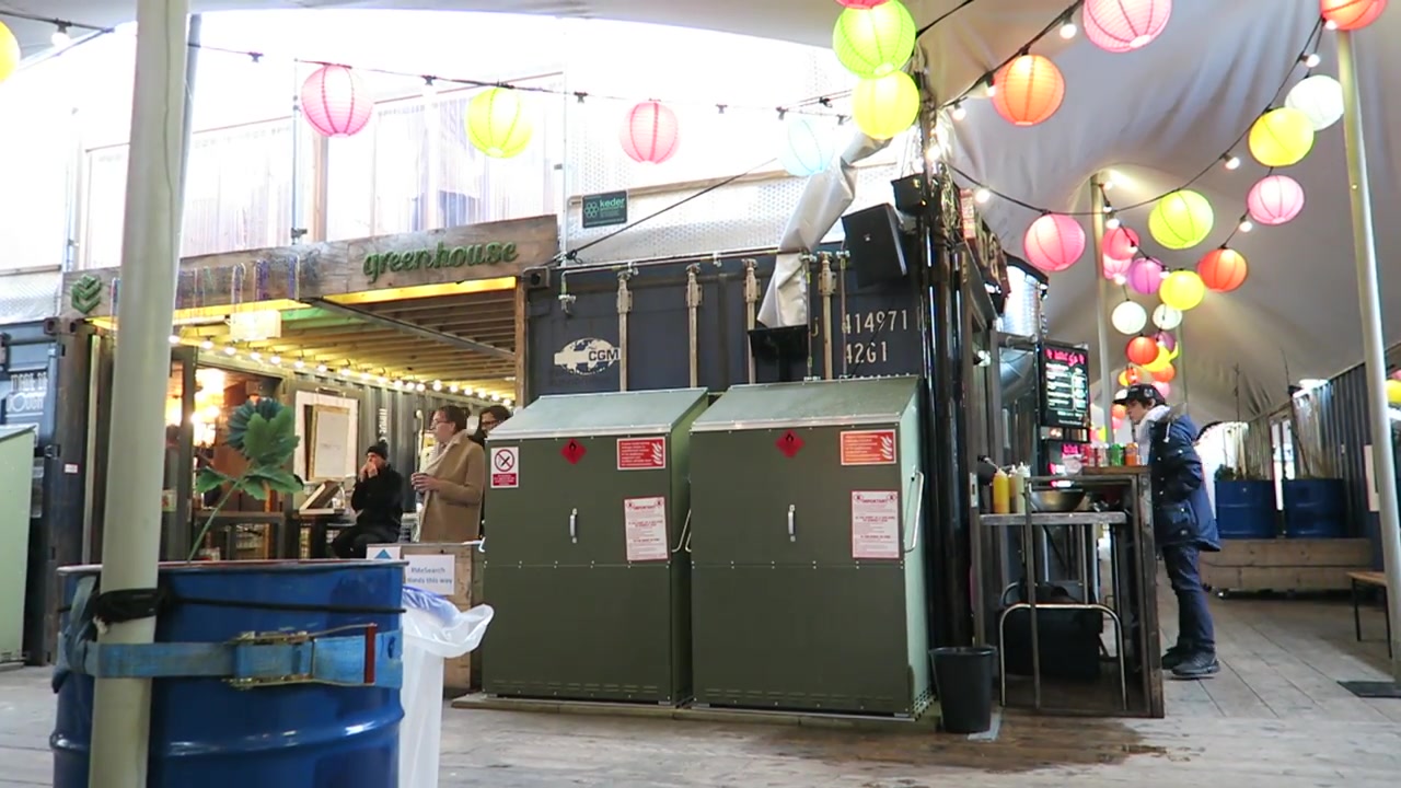 Shared outdoor tables beneath lanterns among the Pop Brixton containers