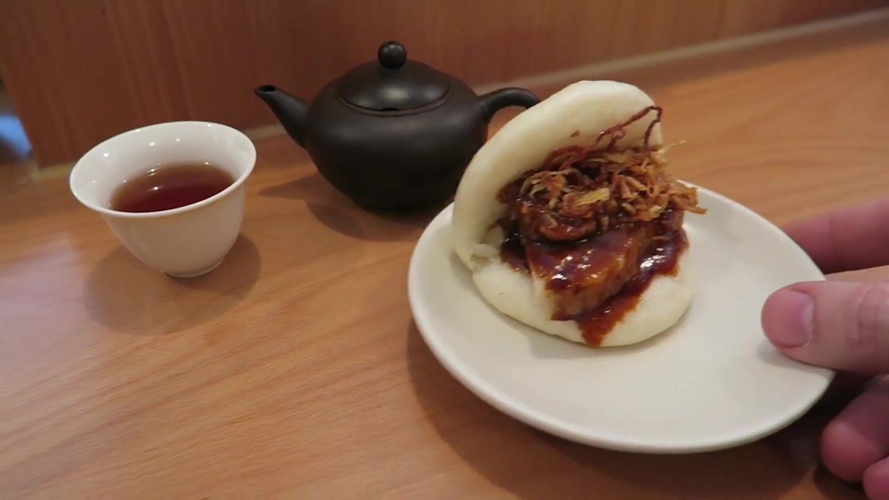 Confit pork bao with crisp shallots beside a cup of tea