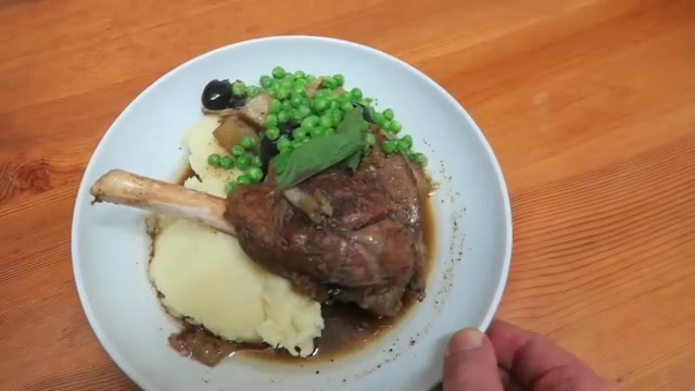Cooked lamb shank served with mashed potatoes and peas.