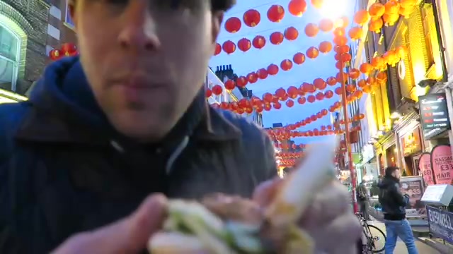 Barry holding an opened pork bun beneath red lanterns in London Chinatown.