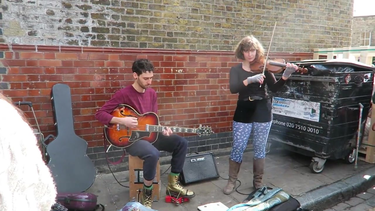 Guitarist and violinist performing beside a brick wall near Columbia Road