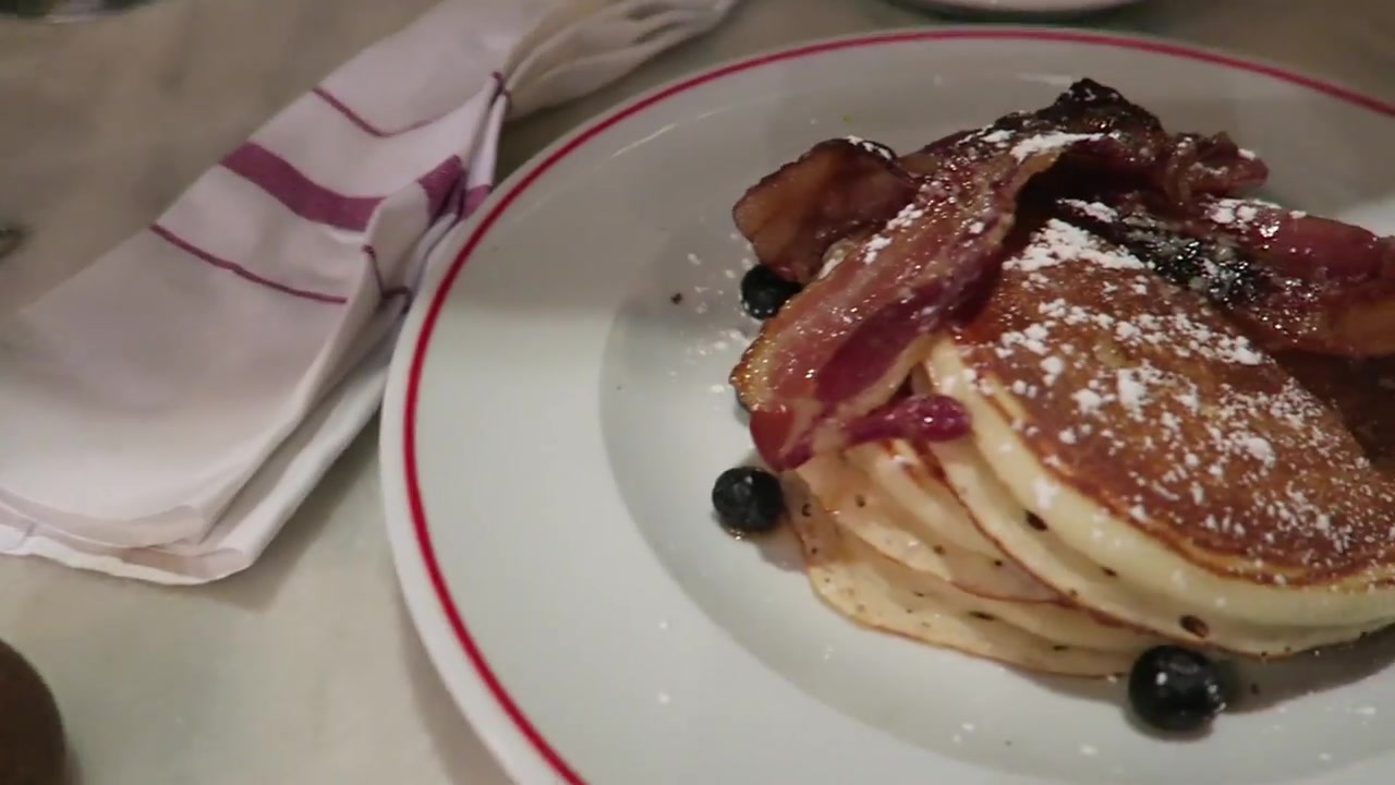 A stack of American-style pancakes with crispy bacon, blueberries and icing sugar at Jackson & Rye Soho.