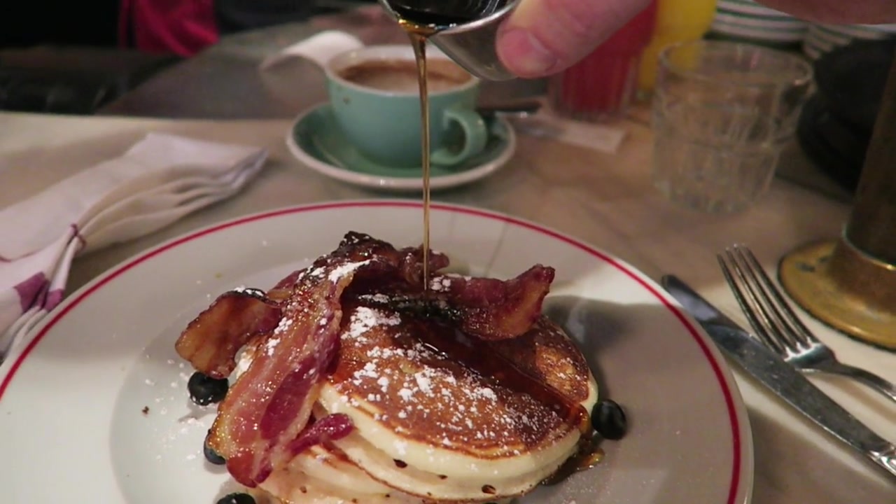 Maple syrup being poured over pancakes topped with bacon and blueberries at Jackson & Rye.