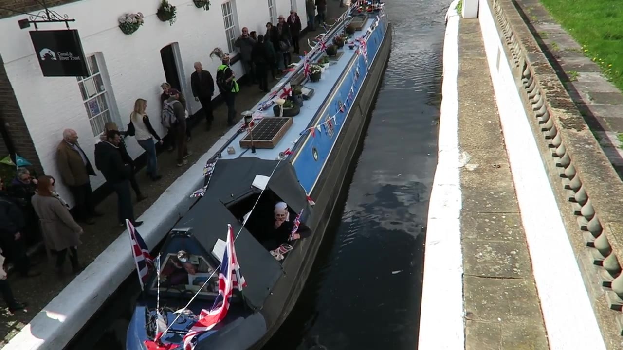 A narrowboat decorated with Union flags approaching a bridge