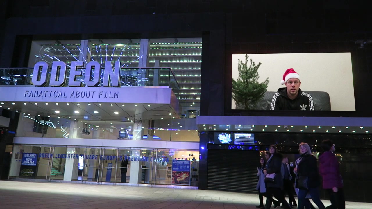 Robert beside his Christmas tree, edited onto the screen outside the Odeon.